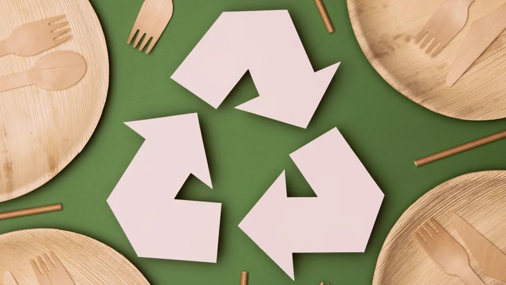 Representação do símbolo de reciclagem em um fundo verde com pratos e utensílios de madeira, enfatizando a importância da sustentabilidade e do descarte consciente.