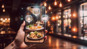 Smartphone exibindo pratos de comida em um ambiente de restaurante iluminado. O uso da tecnologia para compartilhar experiências gastronômicas é evidenciado por elementos virtuais.